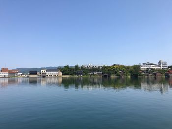 Buildings by lake against clear blue sky