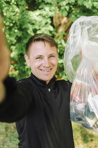 Portrait of smiling coach taking selfie with garbage bag
