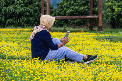 Rear view of person using mobile phone on yellow flowering plants