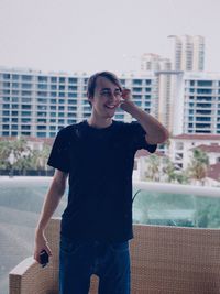 Smiling man standing by seat against swimming pool