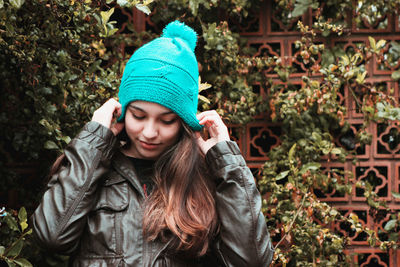 Close-up of young woman wearing turquoise knit hat while standing against plants