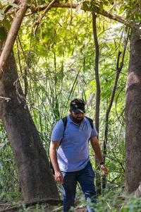Full length of man standing by tree trunk in forest
