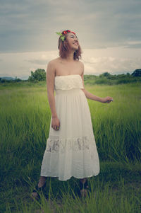 Happy young woman standing on grassy field against cloudy sky