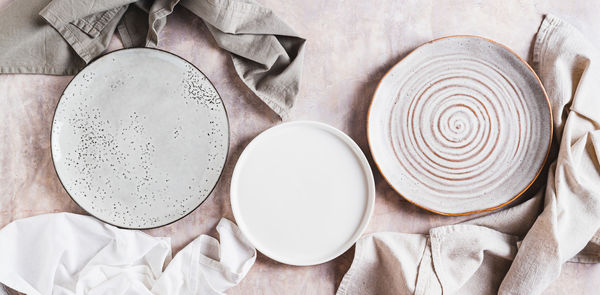 Three empty ceramic plates and napkins on light background top view web banner