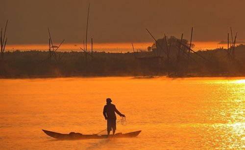 Silhouette man fishing in river against sky during sunset