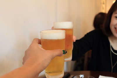 Cropped image of hand toasting beer glass with friend at restaurant