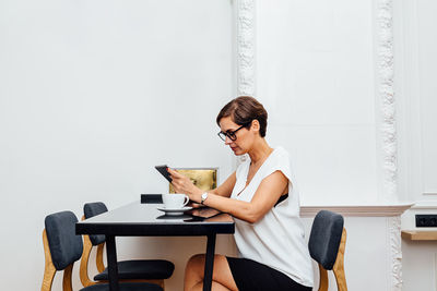 Mid adult woman using smart phone sitting by table at home