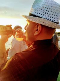 Close-up of man using phone while having drink at beach during sunset