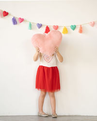 Little girl in red tutu holding pink plush heart pillow over face