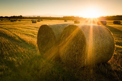 Hay bales on field against sky during sunset