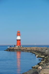 Lighthouse by sea against clear sky