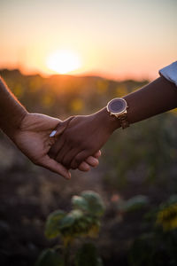 Close-up of couple holding hand against sky during sunset