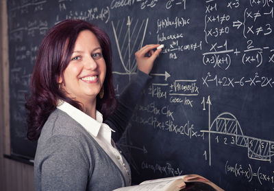 Portrait of smiling teacher writing on blackboard in classroom
