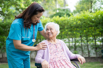 Doctor caregiver help and care asian senior woman patient sitting on wheelchair in park