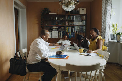Cheerful parents working while sitting with children studying at home