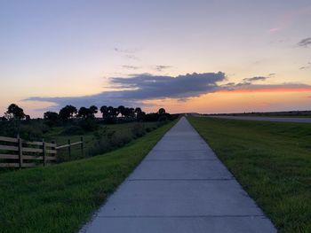 Footpath amidst field against sky during sunset