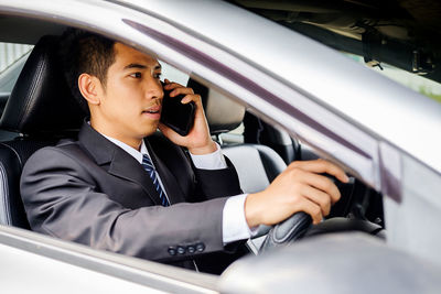 Side view of businessman talking on mobile phone while driving car
