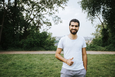 Portrait of smiling young man gesturing thumbs up while standing on grassy field