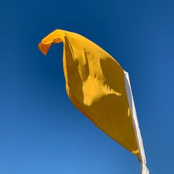 Low angle view of yellow flag against clear blue sky