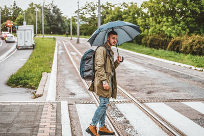 Man with umbrella on a rainy day. handsome young tourist with backpack is crossing the road.