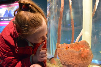 Girl looking at clown fish in coral at aquarium