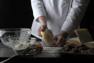 Midsection of chef kneading dough against black background