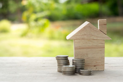 Close-up of wooden model home with coins on wooden table against plants