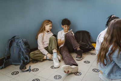 Boy and girl studying together while sitting near wall in school building