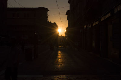 Street amidst silhouette buildings against sky during sunset