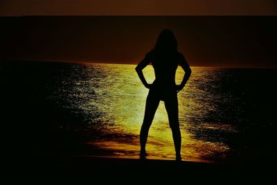 Silhouette woman standing on beach against sky during sunset