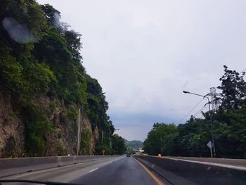 Road by trees against sky