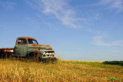 Abandoned car on field against sky