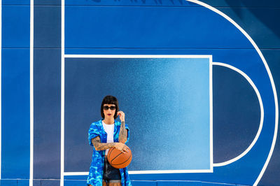 Caucasian girl with sunglasses and tattoos on a blue background with a basketball