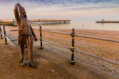 Woman standing on railing by sea against sky