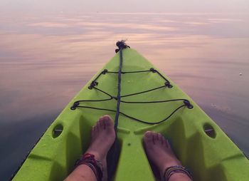 Low section of woman on rowboat in lake during sunset