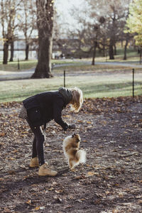 Full length side view of woman playing with pomeranian at park