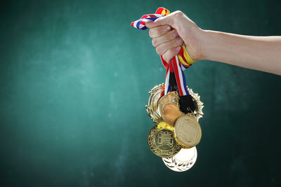 Cropped image of hand holding medals against wall