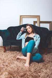 Portrait of woman holding camera sitting by sofa at home