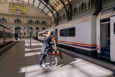 Young woman holding push scooter embracing friend at railroad station