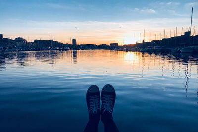 Low section of person over lake against sky during sunset