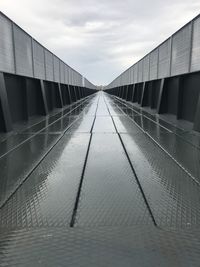 Footbridge over footpath in city against sky