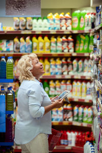 Side view of senior woman holding digital tablet while standing at store