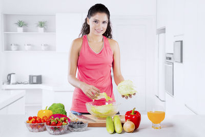 Portrait of smiling woman making salad while standing at home