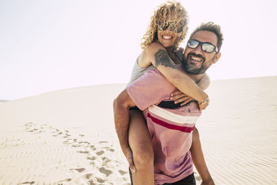 Man carrying woman while walking at beach against clear sky