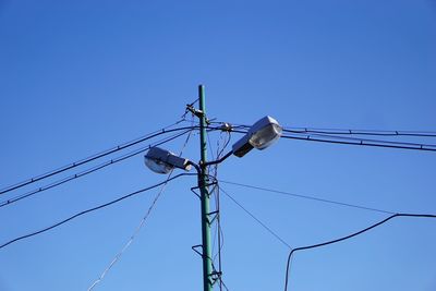 Low angle view of bird perching on electricity pylon against blue sky