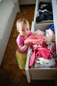 Upper view of little cute baby playing with clothes in the drawers, making order