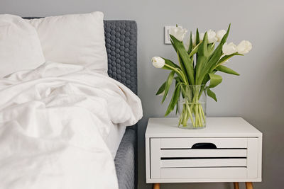 White fresh tulips in a vase near the bed close-up in modern bedroom. spring home decor