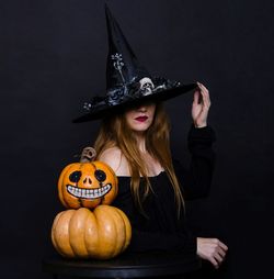 Woman with pumpkins wearing witch hat against black background