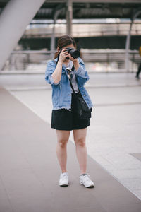 Full length of woman photographing while standing on footpath