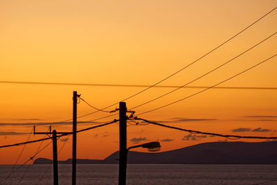 Power lines against sky during sunset